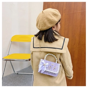Detail of a purple tweed girl's handbag with pearl handle and ribbon on a young model