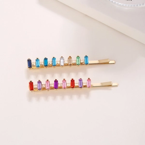 Close-up of golden hair clips with vibrant multicolored crystals in a square cut design