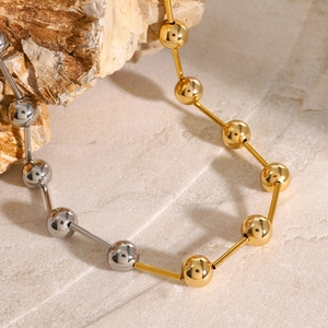 Close-up of gold and silver mixed beaded necklace on a textured stone surface