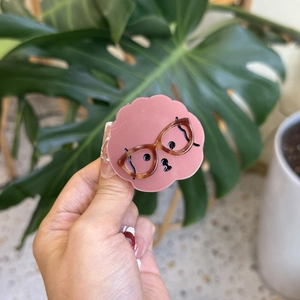 Cute pink acetate hair claw with cartoon puppy and glasses, held in a natural indoor setting