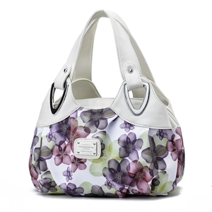 Detail of floral printed fabric tote bag with white leather handle and metal logo plaque