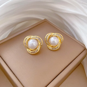 Close-up of golden pearl earrings with crystal halo on brown display box with silk cloth