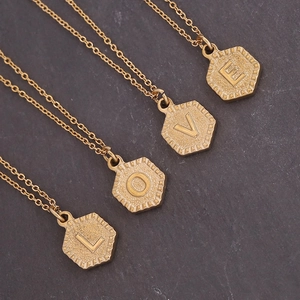Gold stainless steel necklace set with hexagonal LOVE initial pendants on stone surface