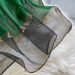 Elegant green and black silk scarf with golden bead edge displayed on white fur