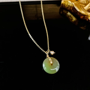 Détail d'un pendentif en jade vert avec fil doré et perle blanche sur une chaîne dorée