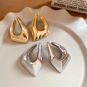Détail de boucles d'oreilles géométriques dorées et argentées brillantes sur plateau en céramique