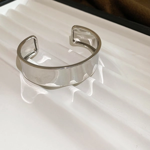 Gros plan d'un large bracelet manchette en argent poli sur un support ondulé blanc