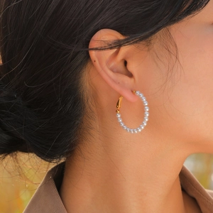 Close-up of elegant gold C-shaped hoop earrings featuring lustrous white pearls on a model