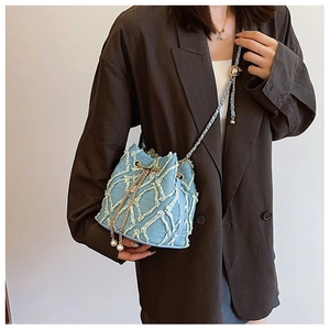 Close-up of blue denim bucket bag with gold chain and pearl charm on a model in a suit