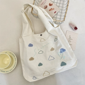 Close-up of tufted cloud embroidery and brand logo on a cream cotton canvas tote bag