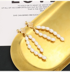 Detail of long drop earrings featuring white rice pearls and gold-plated metal base