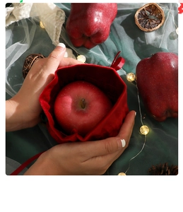 Hands holding a red velvet Christmas apple drawstring gift bag with festive lights