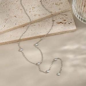 Detail of silver chain necklace with zircon pendants on natural stone and beige surface