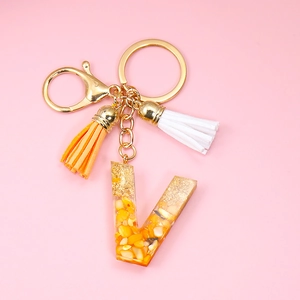 Detail of resin letter V keychain with orange stone chips, gold foil and colorful tassels