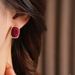 Close-up of a model wearing a dark red flocked oval earring with a golden metal border