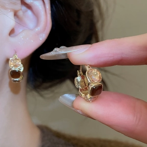 Close-up of gold hoop earring with tiger eye brown stones held by fingers and worn by model