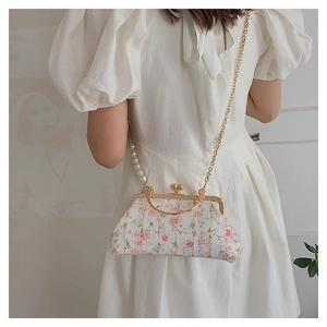 Detail of floral embroidery on a shell-shaped bag with pearl strap and gold chain