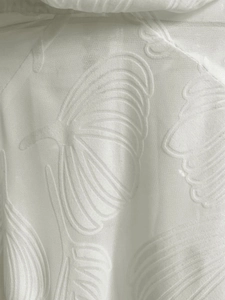 Close-up of white semi-transparent fabric with embossed leaf patterns and textured weave