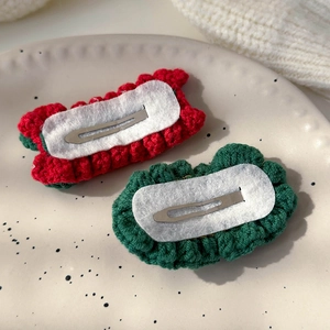 Detail of handmade knit Christmas tree hair clips with red and green yarn on a ceramic tray
