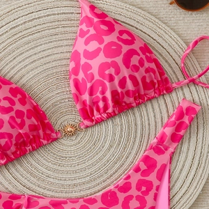 Detailed flat lay of pink leopard print bikini with a gold sun buckle on straw mat