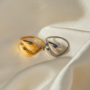 Close-up of gold and silver teardrop crossover rings on elegant silk fabric background