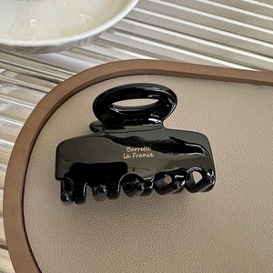 Macro view of a glossy black hair claw clip with gold lettering on a beige leather tray