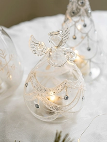 Macro detail of glowing glass angel ornament with white glitter and LED warm lighting