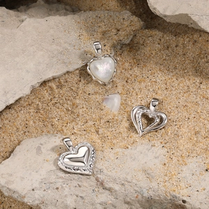 Three S925 sterling silver heart pendants with white mother-of-pearl on beach sand