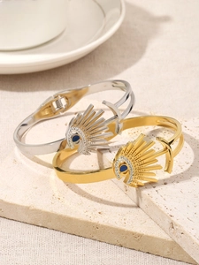 Detail of gold and silver evil eye bracelets with blue stones on a beige stone surface