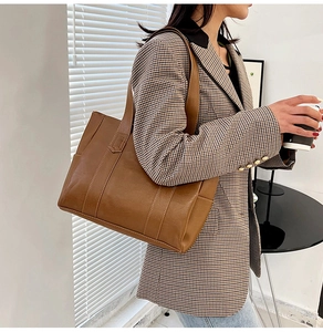 Brown PU leather tote bag styled with a plaid blazer in a professional indoor setting