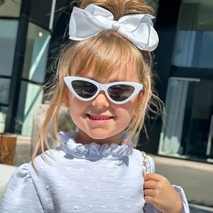 Detail view of girls white cat-eye sunglasses and large satin bow headband accessory