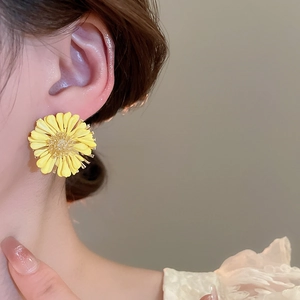 Close-up of yellow raffia daisy stud earring worn on ear for seaside vacation look