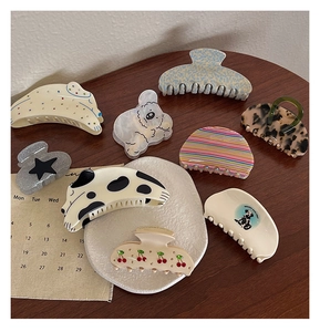 Flat lay of multiple acetate hair claws with cherry patterns and puppy designs on wood