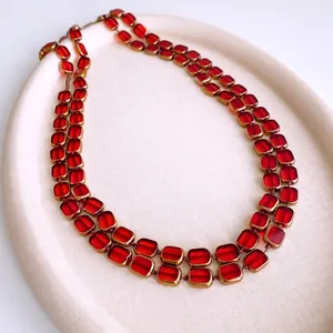 Elegant double-layered gold necklace with ruby-red rectangular glass stones in a tray