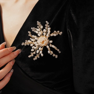 Macro shot of handmade floral pearl brooch with gold wire weaving on dark fabric