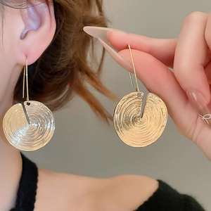 Close-up of golden round drop earrings with textured concentric rings worn by model
