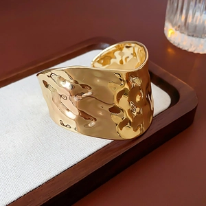 Gros plan sur la texture martelée irrégulière dorée d'un large bracelet jonc ouvert