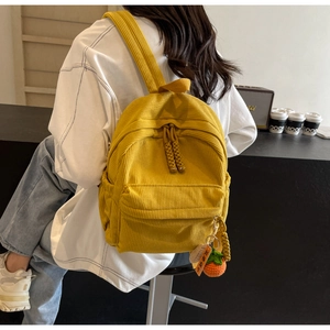 Detail of yellow corduroy backpack with shoulder strap and a cute persimmon charm accessory