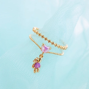 Golden stackable ring set with pink heart stone and purple bear charm on blue tulle
