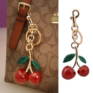 Close-up of glittery cherry bag charm with gold clasp on a luxury leather handbag