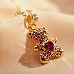 Golden necklace featuring a cute bear pendant with red heart crystals on beige fabric