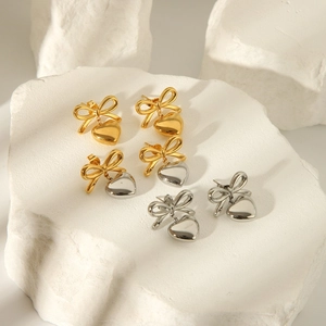 Elegant 18K gold and silver butterfly bow heart drop earrings on stone background