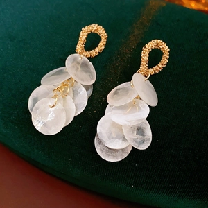 Detail of bohemian gold oval hoop earrings with white translucent round shell fringe