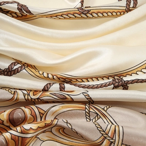 Elegant off-white silk-like scarf with golden chain and rope patterns in smooth folds