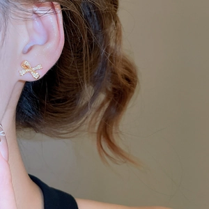 Close-up of golden bow stud earrings with sparkling zircons worn by a female model