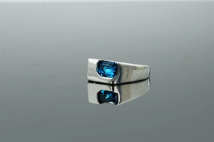 Close-up of polished wide band ring featuring a rectangular blue sapphire stone and reflection