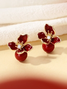 Macro detail of red enamel flower earrings with gold edges and a large crimson bead drop