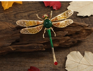 Detailed view of dragonfly brooch with golden wings and green gemstone on wood