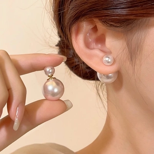 Elegant gold double pearl stud earrings with large and small pearls worn by a model