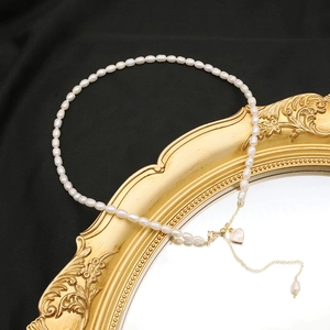 Detailed close-up of a white pearl necklace with a gold heart pendant on a vintage mirror